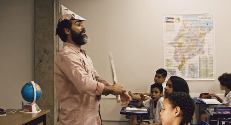 Temos um professor, dando um aula de maneira dinâmica, incorporando personagem de um revolucionários,usando um chapéu e uma espada de papel