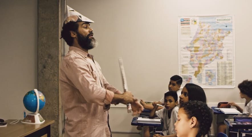 Temos um professor, dando um aula de maneira dinâmica, incorporando personagem de um revolucionários,usando um chapéu e uma espada de papel em Escola Sem Sentido.