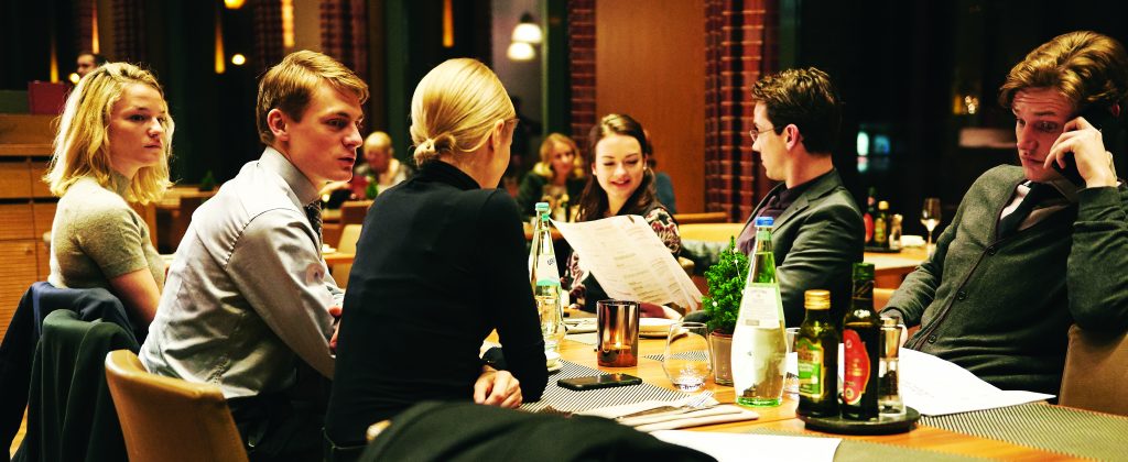 Jovens em uma mesa de jantar, cena do filme o chão sob meus pés. 