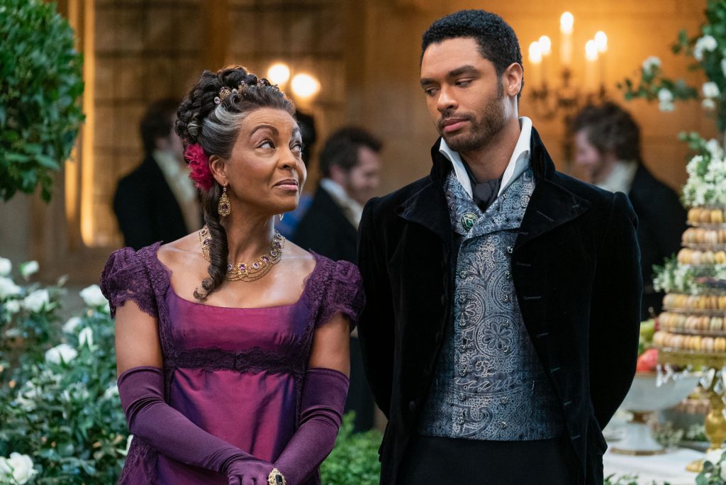 A foto mostra os personagens Lady Danbury (vivida por Adjoa Andoh) e o duque Simon Basset (Regé-Jean Page) da série Bridgerton da Netflix. 