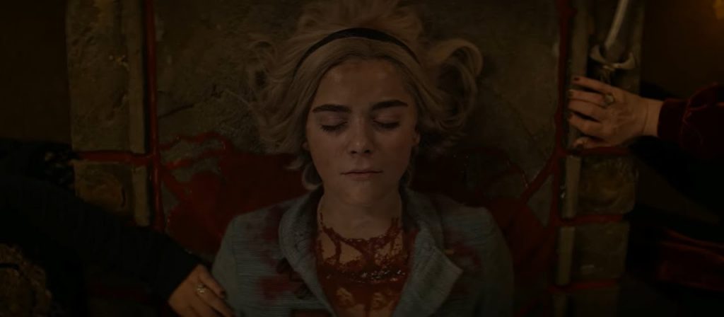 A personagem Sabrina, deita em um altar, coberta de sangue 