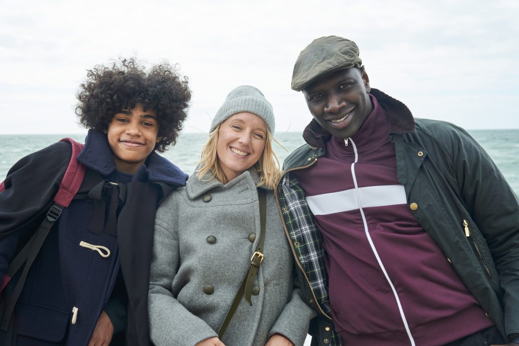 A foto mostra os atores Etan Simon,  Ludivine Sagnier e Omar Sy caracterizados de seus personagens Raoul, Claire e Assane, respectivamente da série Lupin da Netflx. 