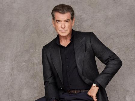 O ator Pierce Brosnan escalado para viver Senhor Destino em Adão Negro de terno posando para uma foto de estúdio. Otageek