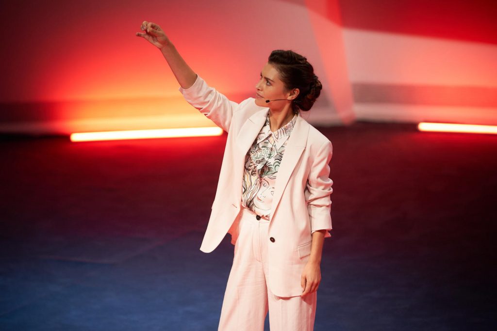 Mulher no centro de um palco com o braço erguido - The One, Netflix