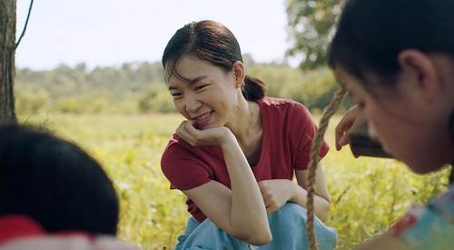 A atriz Han Ye-ri, agachada sorrindo em cena do filme Minari.