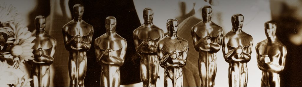 Header do especial do MUBI E o Oscar vai para... Nele, vemos oito estatuetas do Oscar, lado a lado, com flores à esquerda.
