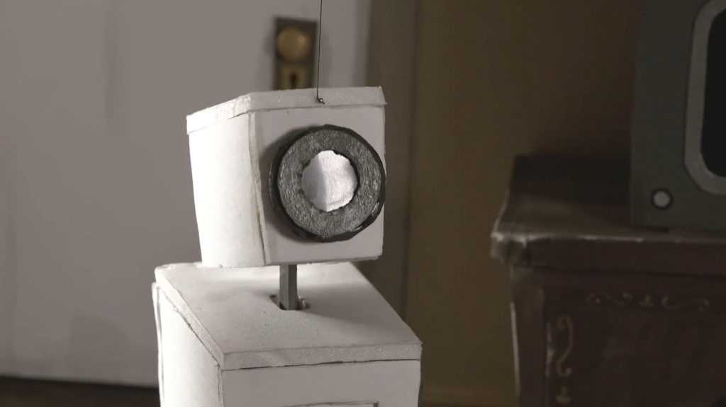 Close do "rosto" do robô olhando para o protagonista que o vê (ao robô) em primeira pessoa.