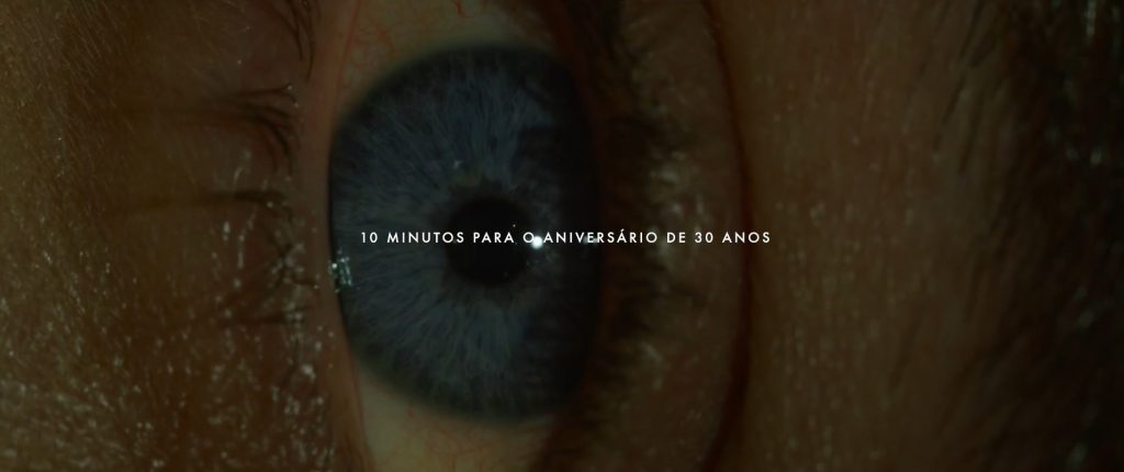 Close de um olho azul visto de lado. Sobre a cena está escrito em branco e em caixa alta: "10 minutos para o aniversário de 30 anos.