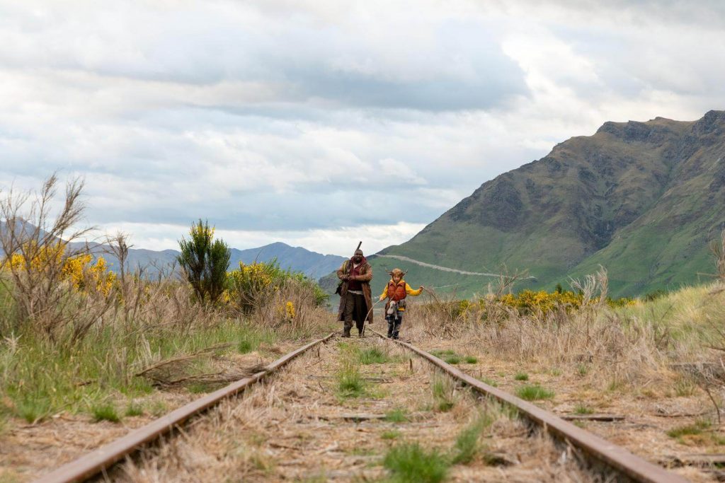 Imagem divulgada da série Sweet Tooth mostra o menino cervo andando ao lado de outro personagem em uma estrada antiga de trem.