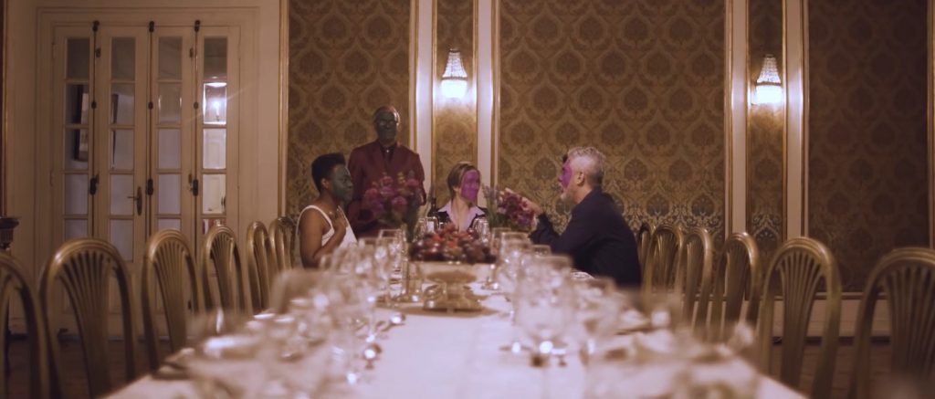 Cena da protagonista, Yeda, de rosto verde sendo entrevistada, durante um jantar, pela burguesia roxa, buscando seu "lugar ao sol". - 1º Festival de Cinema Brasileiro Fantástico