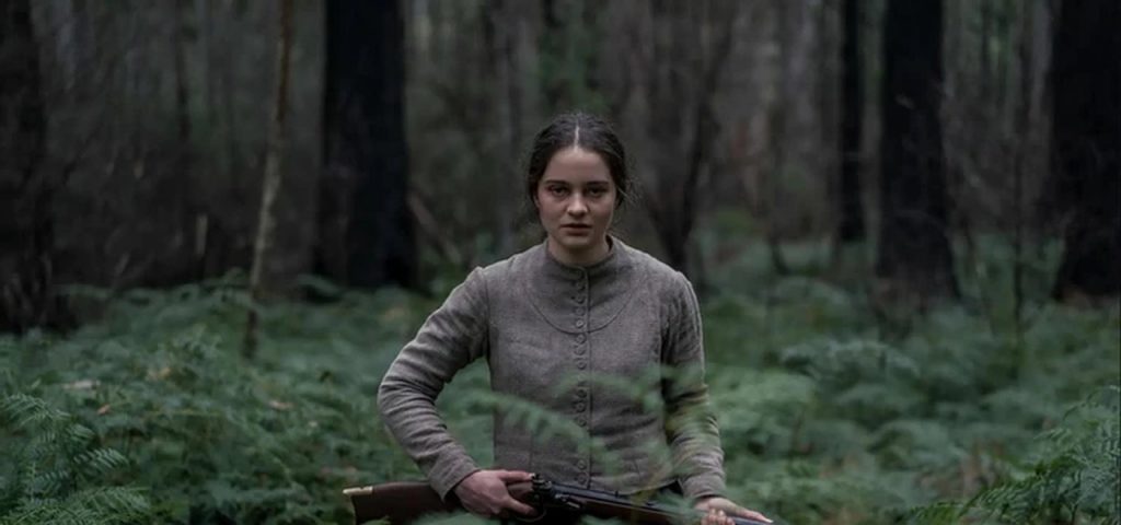 Clare Carroll, personagem de Aisling Franciosi, empunhando uma espingarda em meio a uma floresta. - Otageek