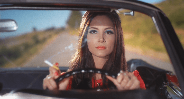 mulher dirigindo um carro, ambas as mãos no volante e cigarro numa delas, expressão séria - Otageek