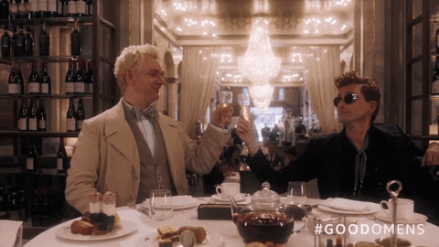 Michael Sheen (Quiz, Staged) e David Tennant (Des, Staged) brindando taças de champanhe em um restaurante