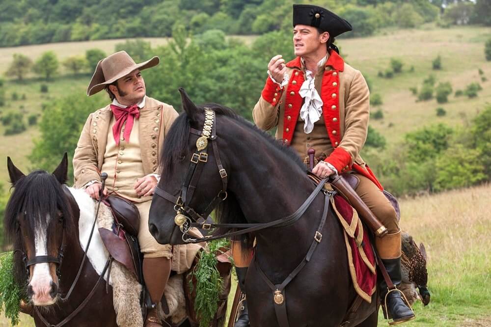 A imagem mostra Gaston e LeFou em cima de cavalos.