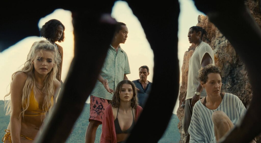 Personagens olham ossos achados na praia no filme Tempo