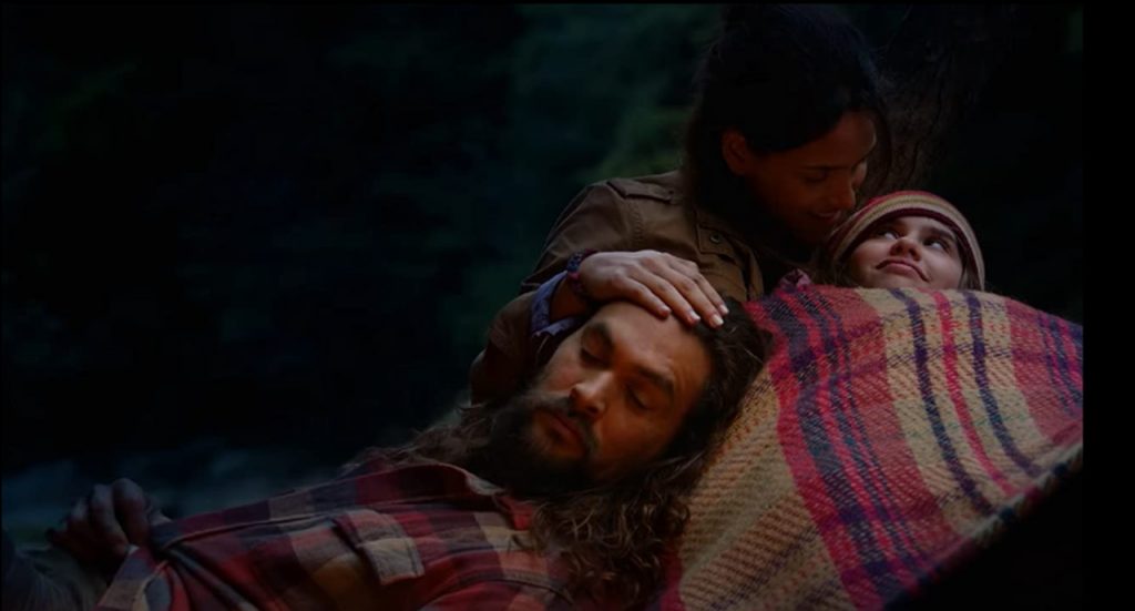 Jason Momoa deitado no colo de sua esposa em cena do filme Justiça em Família