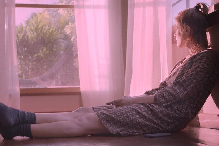 Mulher loira sentada numa janela olhando para o horizonte