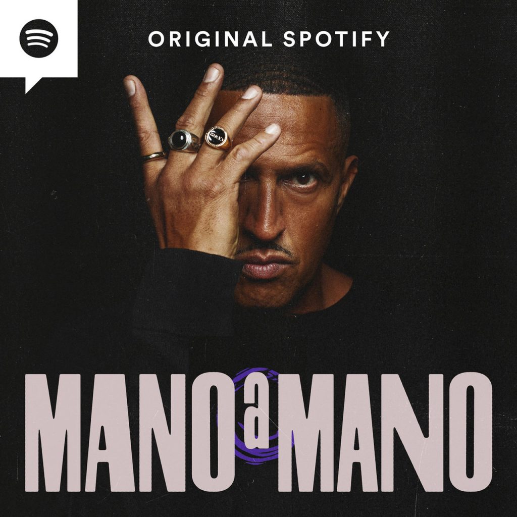 Imagem de capa do podcast Original Spotify Mano a Mano. Nela, no canto superior esquerdo, dentro de um balão de fala branco, encontra-se o logo do Spotify. No centro superior, está escrito "original Spotify". Abaixo, na frente de um fundo preto, está o Mano Brown, com uma roupa de manga comprida preta,com a mão direita tampando parte do rosto. Nos dedos indicador, médio e anelar, ele usa anéis.. Na parte inferior da imagem, um letreiro diz "MANO A MANO". 