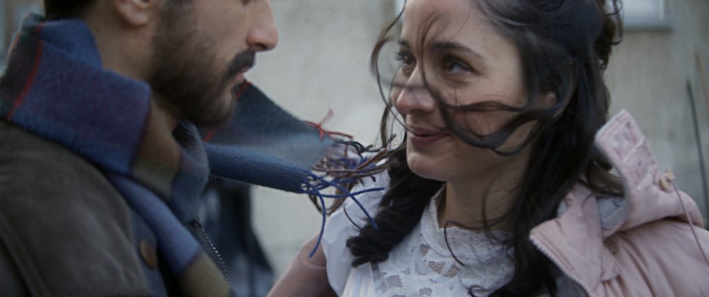 Um homem e uma mulher se olham. O cabelo dela está passando sobre o rosto. Do homem, só vemos do nariz para baixo. Eles estão sorrindo sem mostrar os dentes. Essa imagem é de "O dia que Mudou o Mundo"