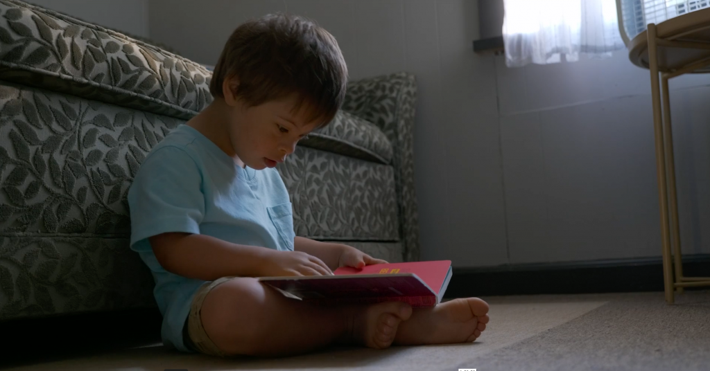 Criança sentada no chão lendo um livro em cena "Um Lugar Para Todo Mundo"