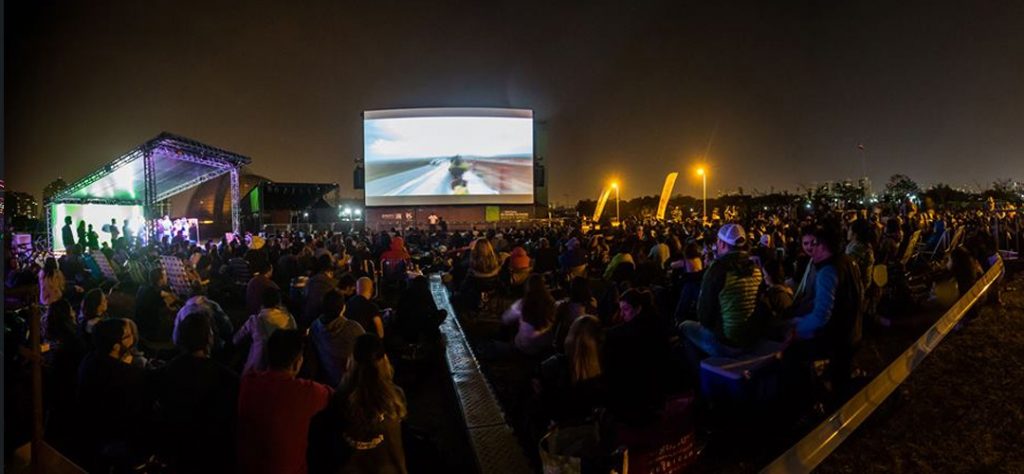 Imagem do Rocky Spirit 2019, com o público assistindo a um filme em um telão durante a noite e ao livre - Otageek