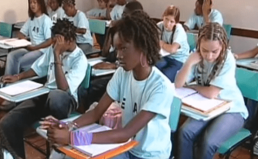 Várias crianças uniformizadas sentas em carteiras na sala de aula