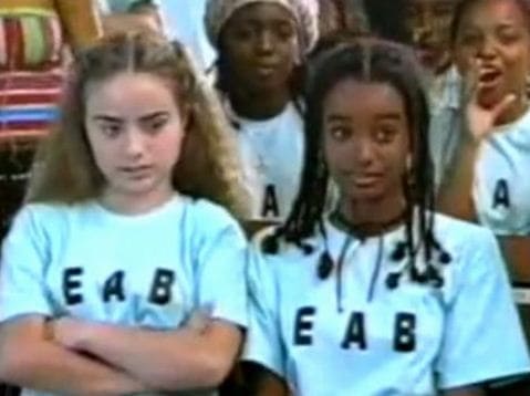 Duas meninas, uma negra e outra branca vestido o mesmo uniforme escolar, elas estão sentadas