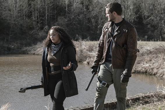 Duas pessoas vestidas de preto com armas andando próximas a um rio