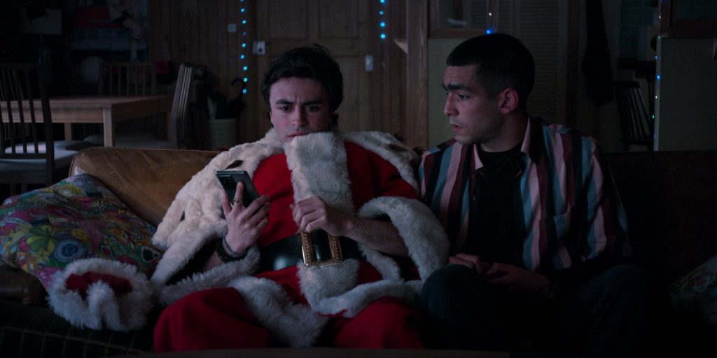 Dois homens sentados no sofá, um deles está vestido de papai Noel e com o celular em mão