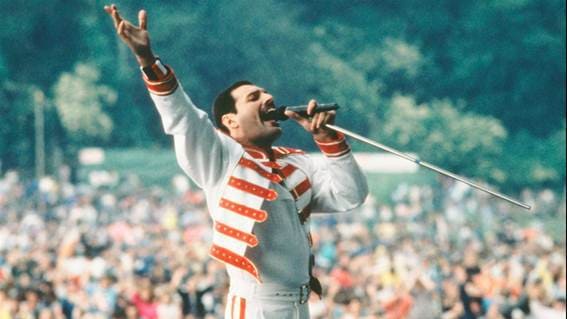 Homem com jaqueta branca e vermelho, cantando diante de um publico