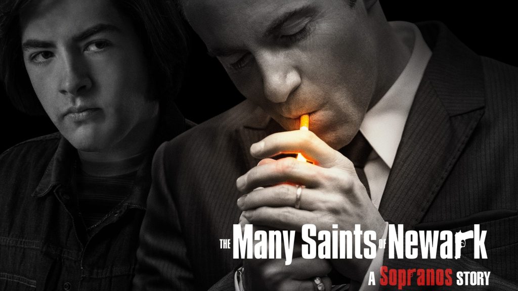 Imagem promocional do filme "The Many Saints of Newark". Nela, vemos à esquerda, o personagem Tony Soprano, olhando para a direita, onde está o seu tio, Dickie Moltisanti, acendendo um cigarro. A imagem está em preto-e-branco, com as únicas cores sendo a palavra "Sopranos" em vermelho em um letreiro no canto inferior direito (que diz "The Many Saints of Newark - A Sopranos Story"), e a luz amarela do fogo do isqueiro sendo acendido por Dickie