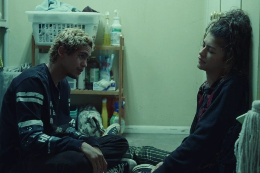 Cena de Elliot (Dominic Fike) e Rue (Zendaya) sentados no chão da lavanderia de uma casa no primeiro episódio da segunda temporada de Euphoria