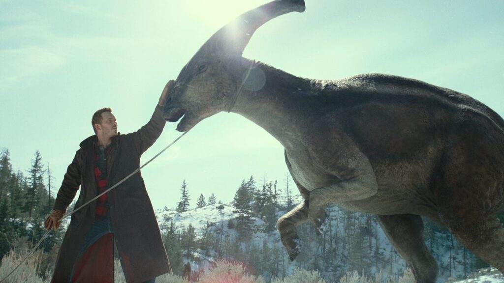 Chris Pratt como Owen em Jurassic World Domínio ao lado de um enorme Parassauro.
