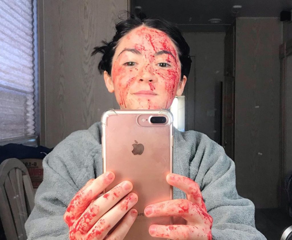 Isabelle Fuhrman tira uma selfie em frente ao espelho de seu camarim de A Órfã 2: A Origem, mostrando seu rosto e suas mãos ensanguentados. 