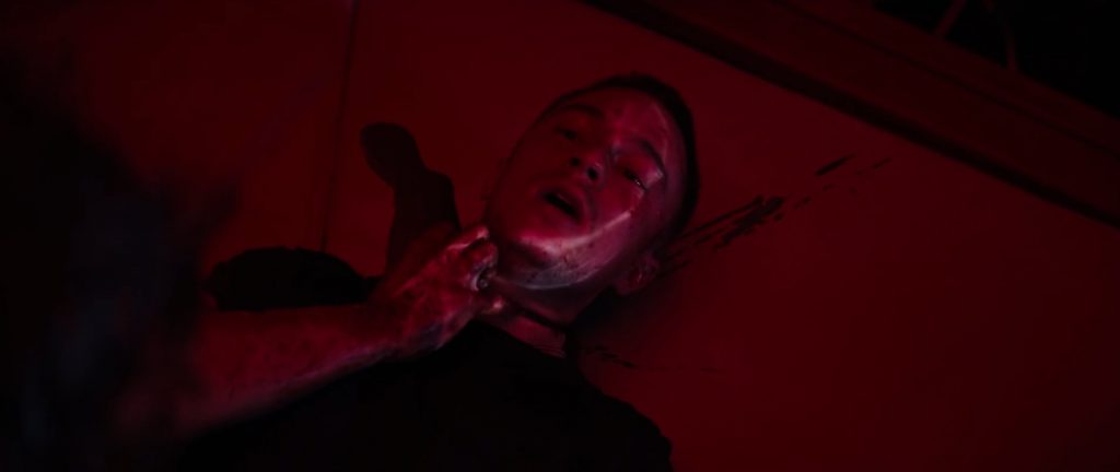 Um rapaz agoniza com a garganta cortada, em uma cena toda vermelha.