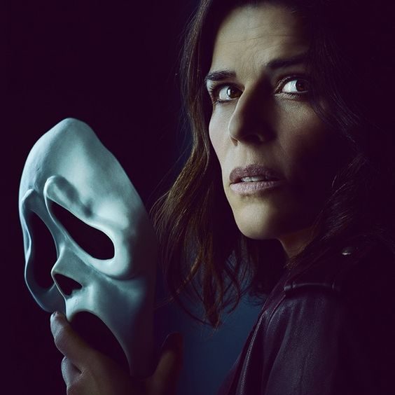 Sidney, uma mulher em seus 40 anos, olhando para trás em quanto segura uma mascara de Ghostface em um shoot promocional para o filme Pânico 5.