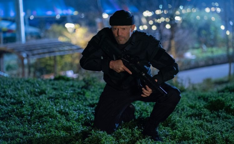 Jason Statham, todo de preto, invade o local onde ocorrerá a cena citada do flashback. otageek