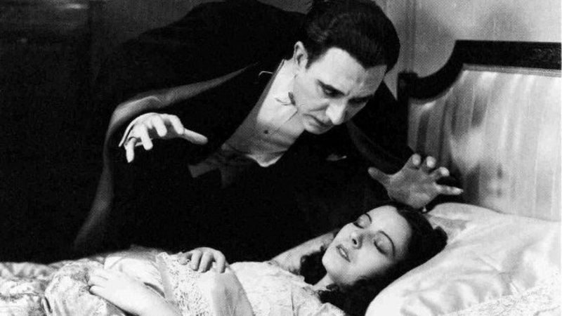 Béla Lugosi interpretando Drácula de 1931 espreita Bunny Beatty, adormecida em seu leito. 