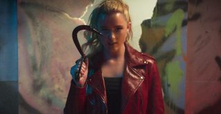 Menina loira com jaqueta vermelha segurando um gancho e coberta com sangue