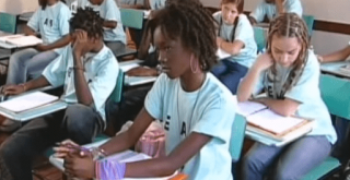 Uma sala de aula, como alunos uniformizados sentados nas carteiras, escrevendo em cadernos. A maioria dos alunos são negros