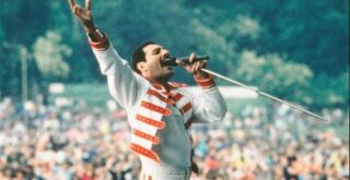 Homem com jaqueta branca e vermelho, cantando diante de um publico